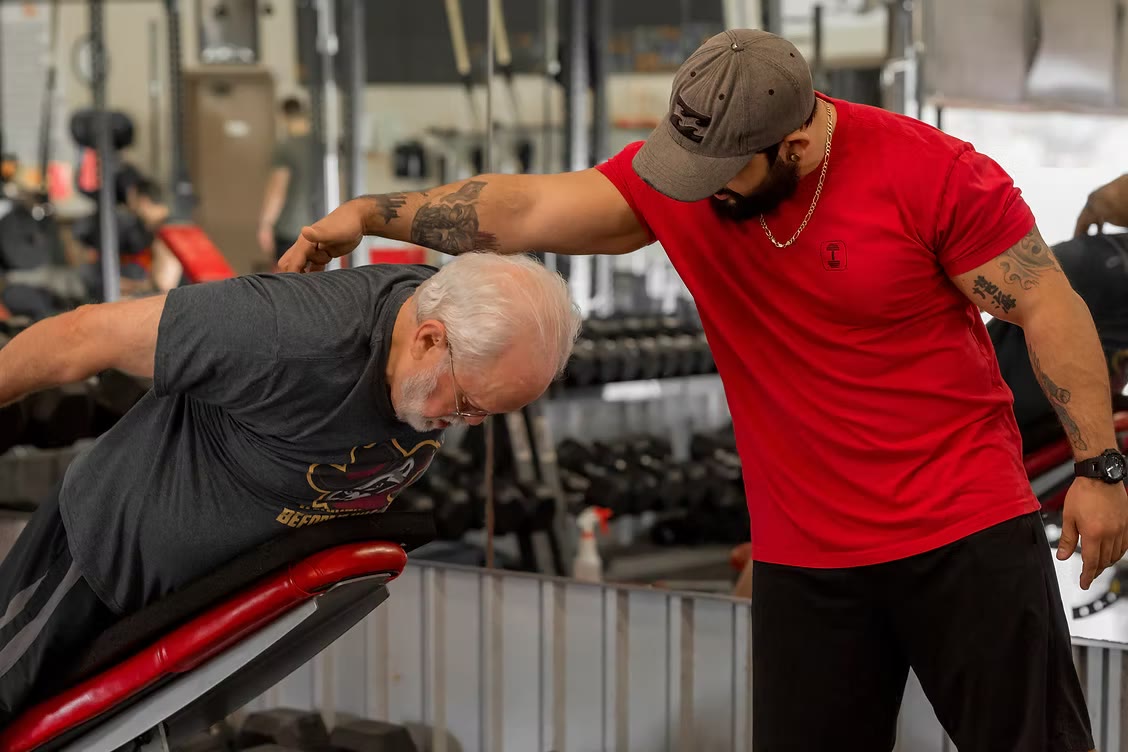 Martin coaching an older client through a bench exercise, one hand guiding his back